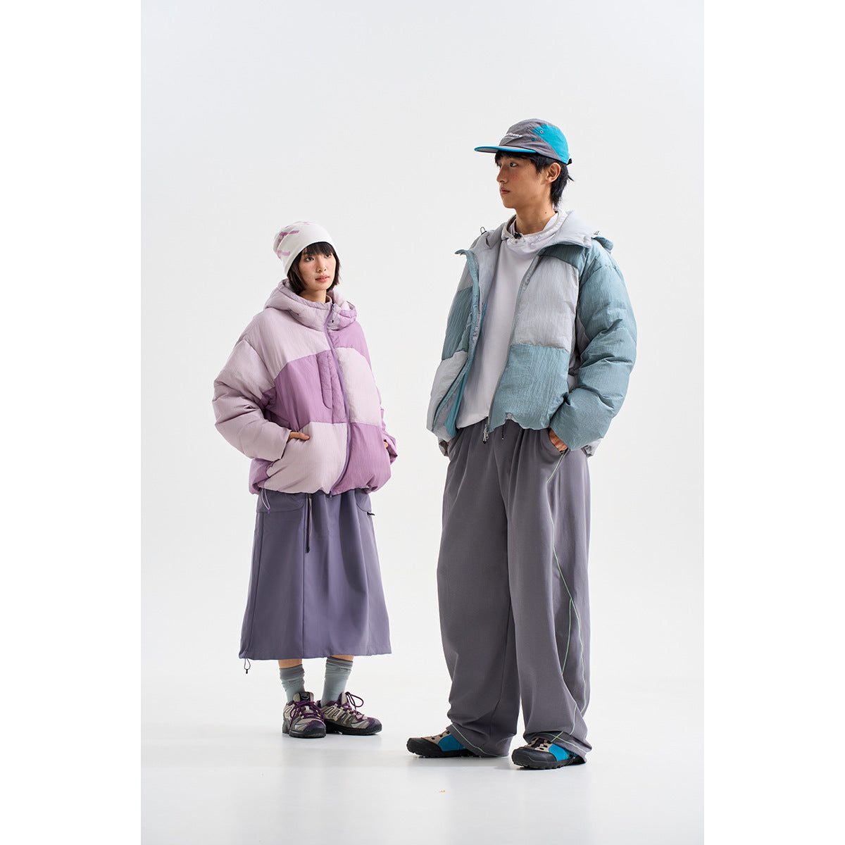 Two models wearing color-block hooded puffer jackets, one lavender and one blue-gray, with loose gray bottoms.
