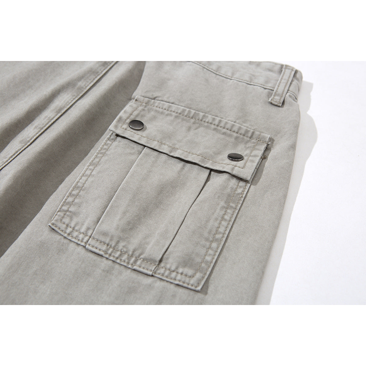 Close-up of a rectangular cargo pocket with a two-snap flap on light gray pants.