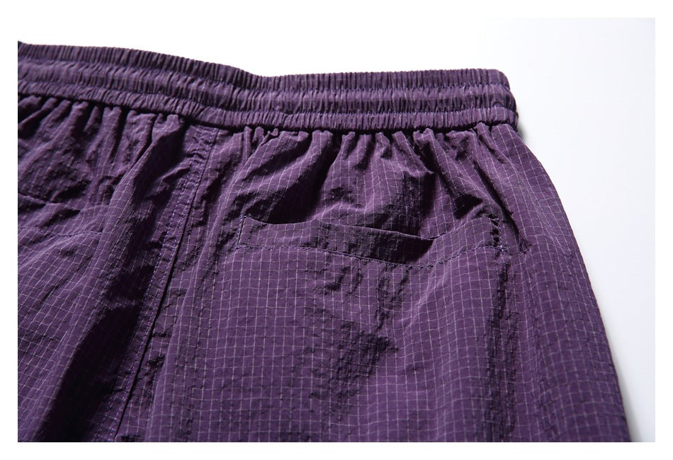 Close-up of purple grid-pattern shorts showing the elastic waistband and a patch pocket.