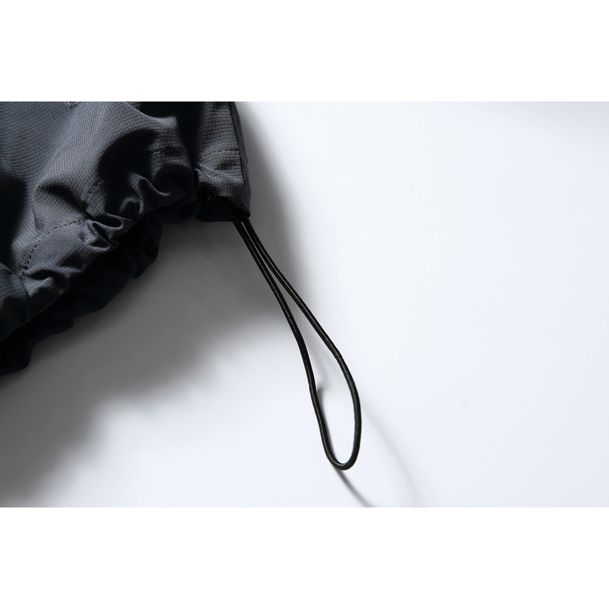 Close-up of a black jacket cuff with gathered fabric and a long looped adjustment cord.