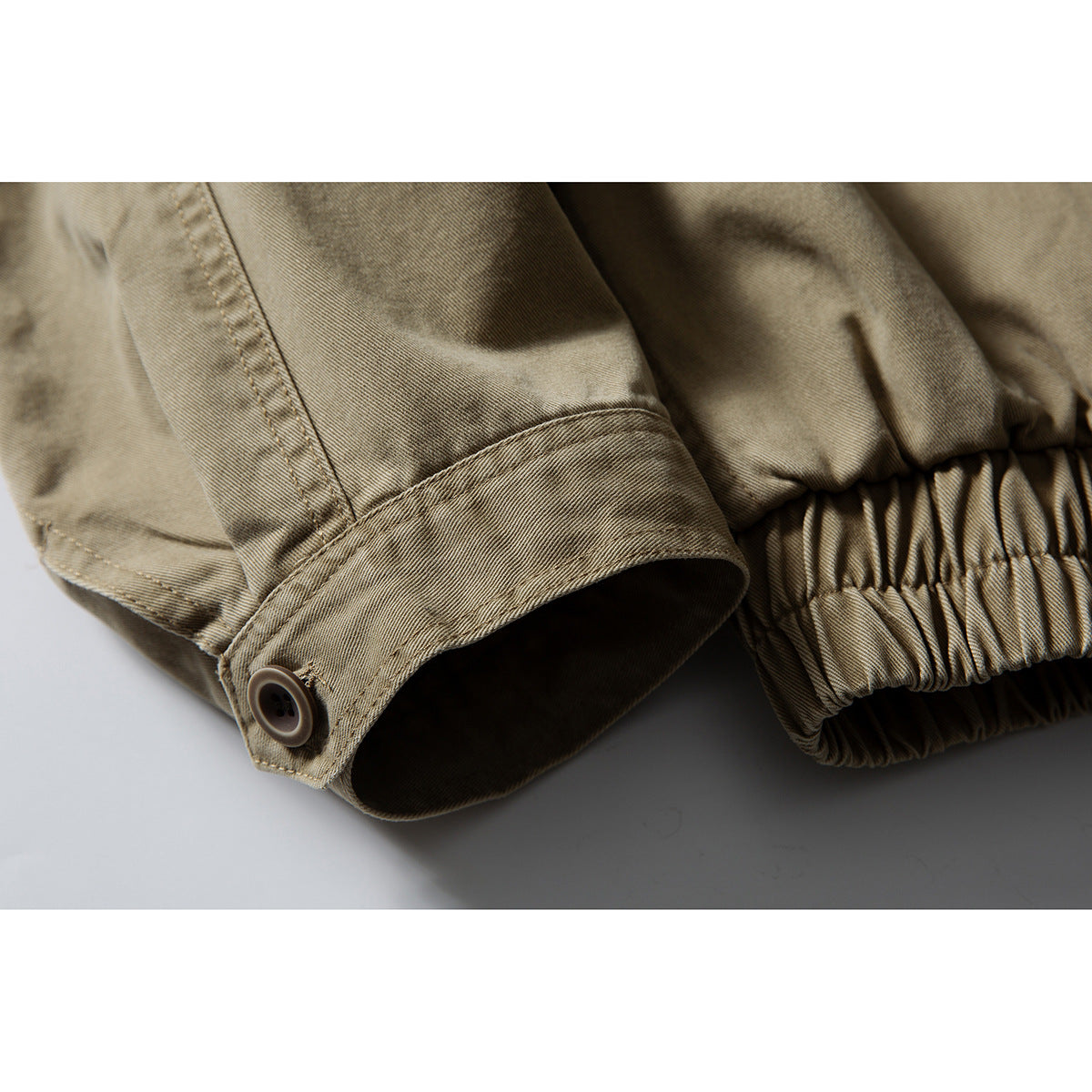 Close-up of an olive-khaki jacket sleeve cuff with a button and gathered elastic hem.
