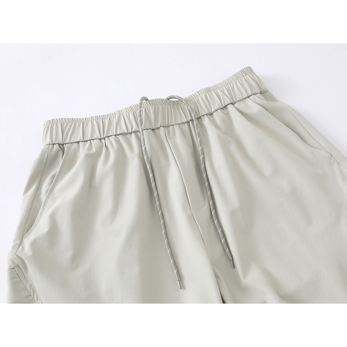 Close-up of light gray wide-leg pants showing the elastic waistband, long drawcords, and side pockets.