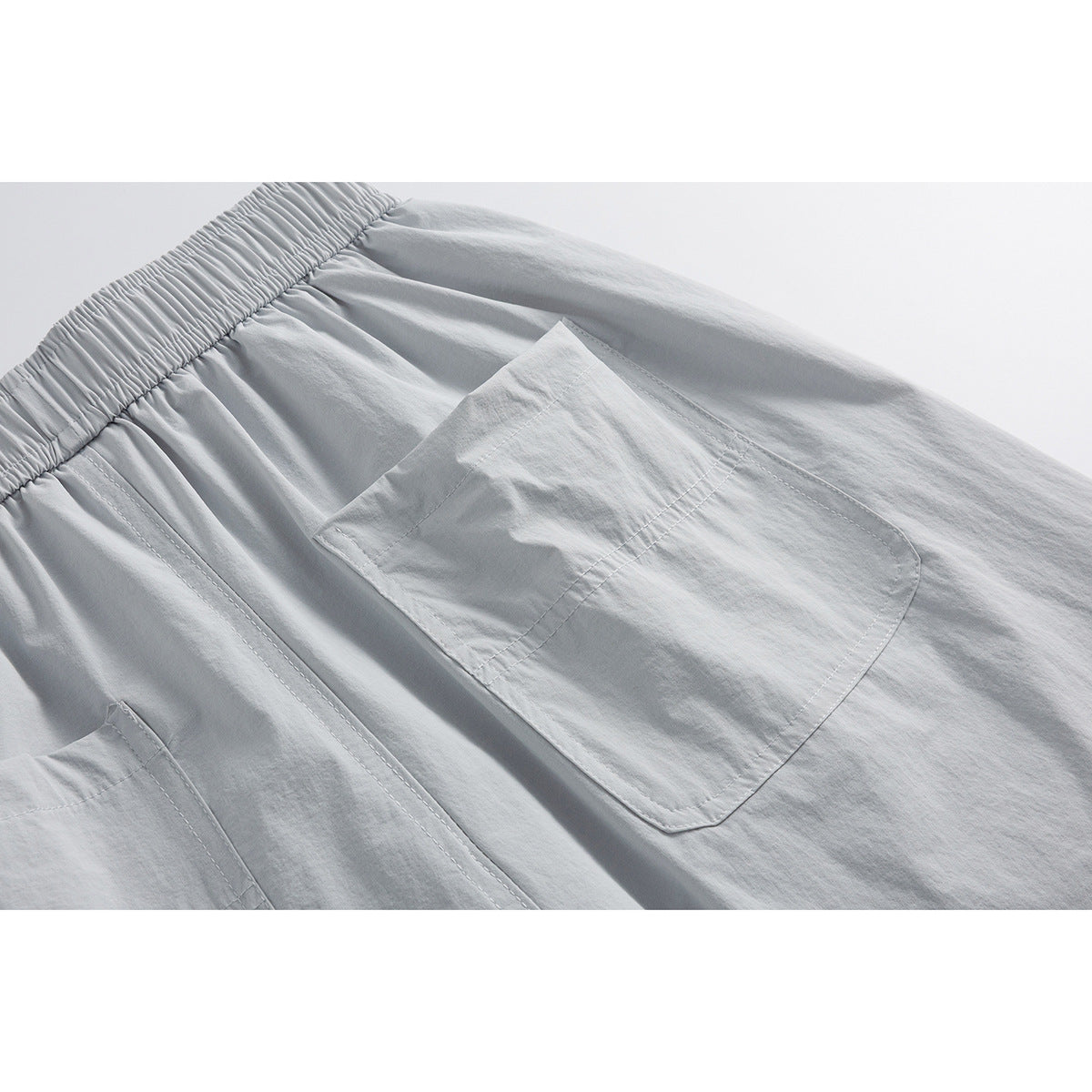 Close-up of light gray shorts showing a large stitched rear pocket and elastic waistband.