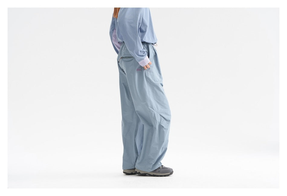 Side view of a model wearing loose blue-gray pants with a zippered pocket and a matching long-sleeve top.