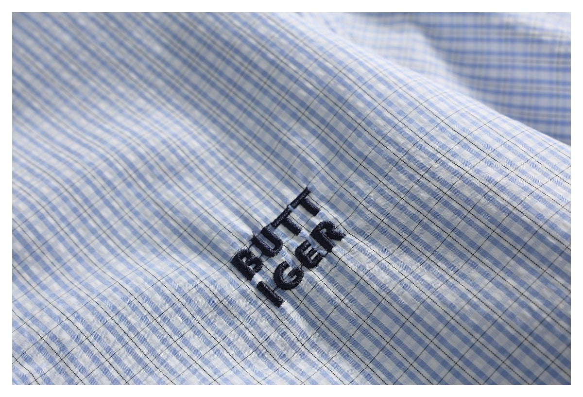 Close-up of dark embroidered lettering on blue-and-white checked shirt fabric.