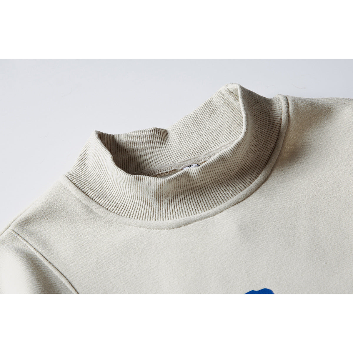Close-up of an off-white sweatshirt's tall ribbed mock neck and shoulder seam.