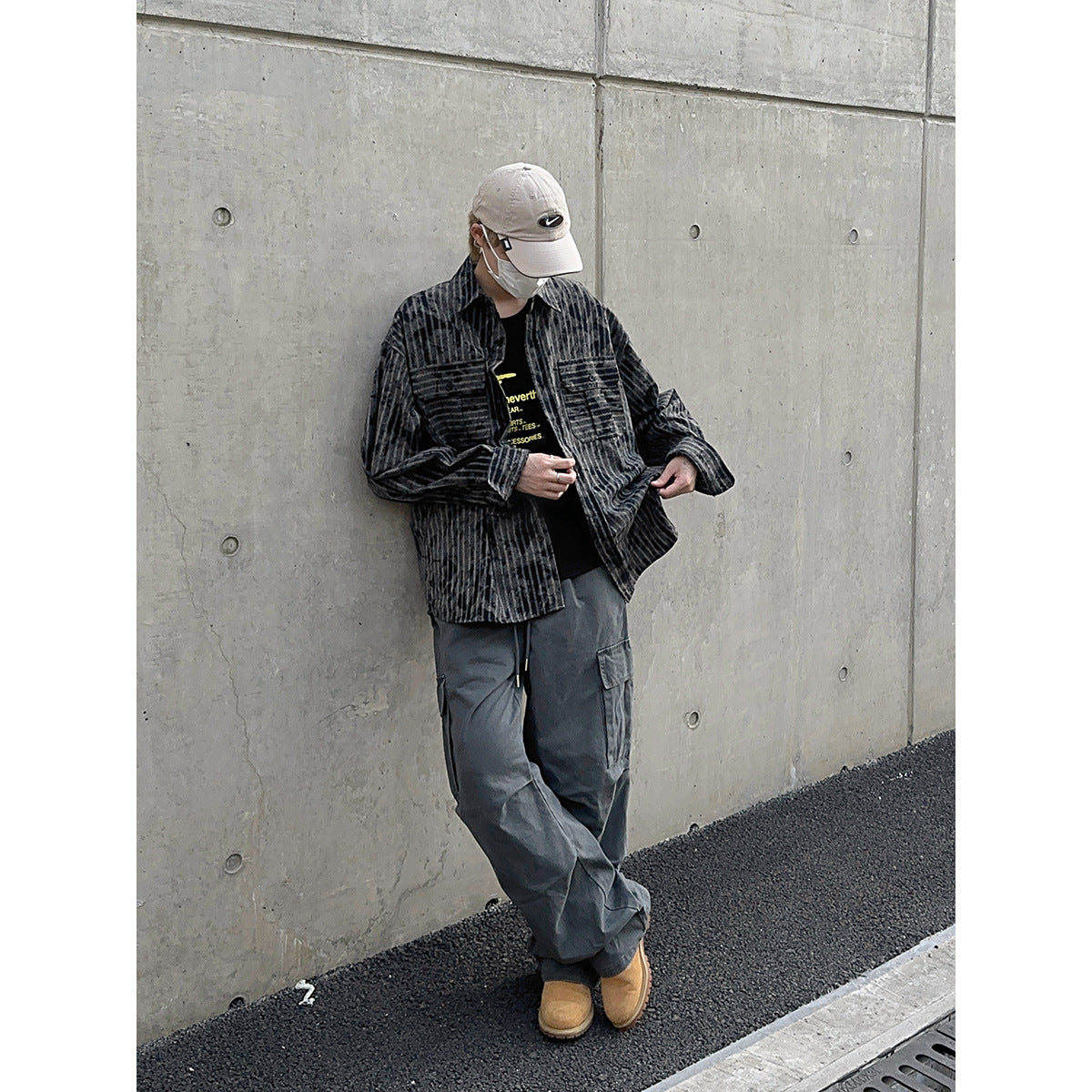 Model wearing a charcoal distressed-stripe button-up shirt over a black graphic tee, with gray cargo pants and tan boots.