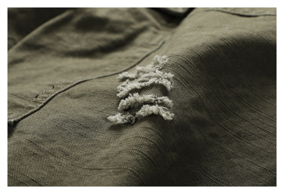 Close-up of olive trouser fabric with a small distressed tear and loose pale threads.