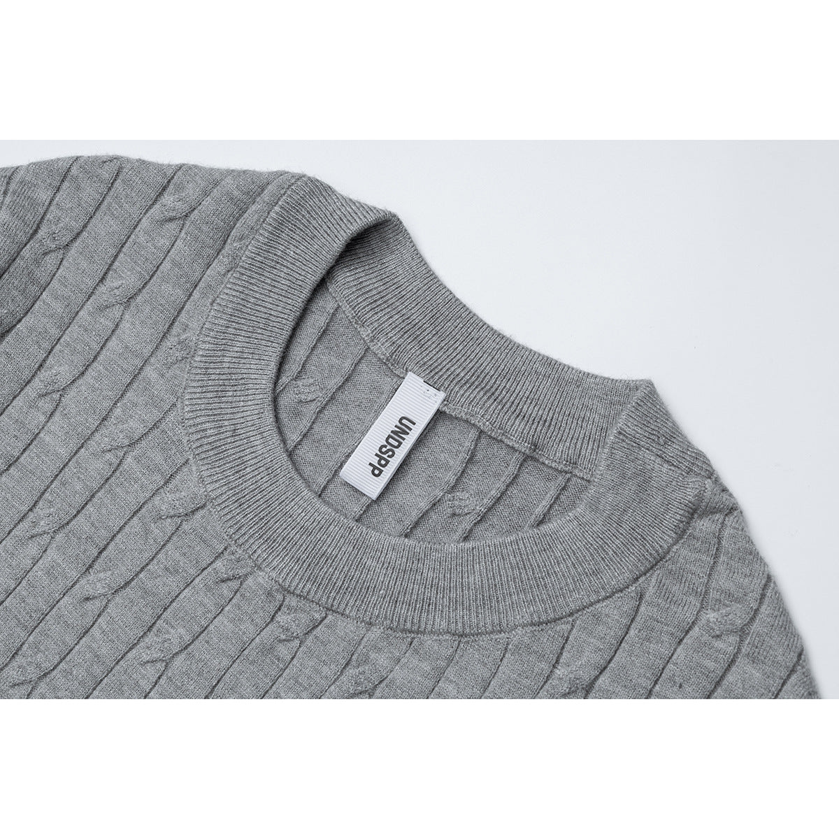 Close-up of a gray cable-knit top's ribbed crew neckline and inner label.