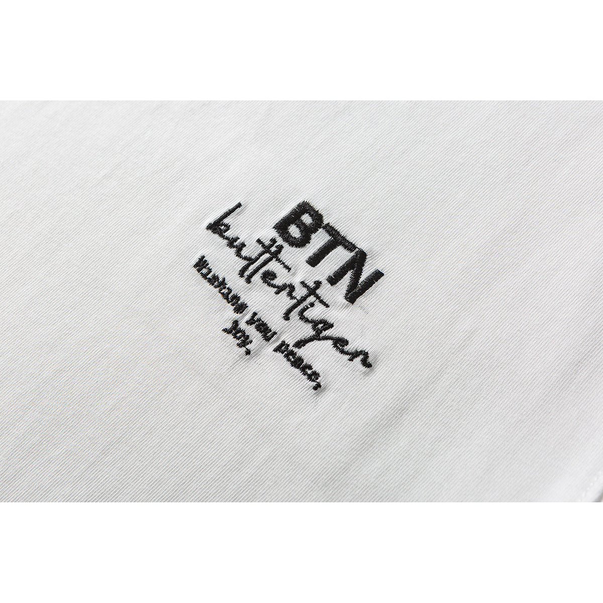 Close-up of black embroidered lettering on white T-shirt fabric.