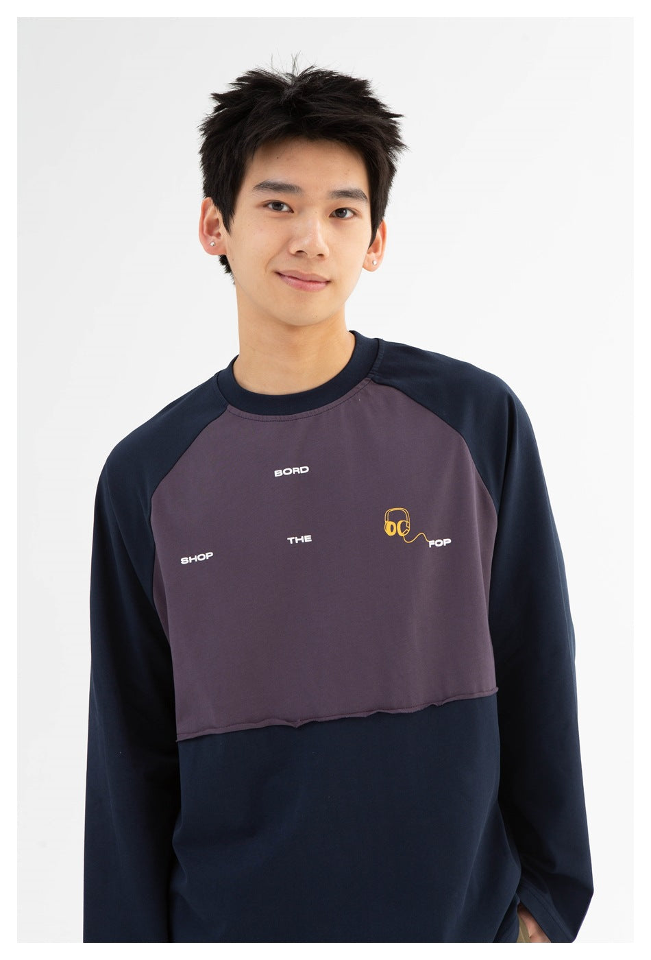 Closer view of a model wearing a navy and muted purple raglan sweatshirt with white chest text and yellow headphone artwork.