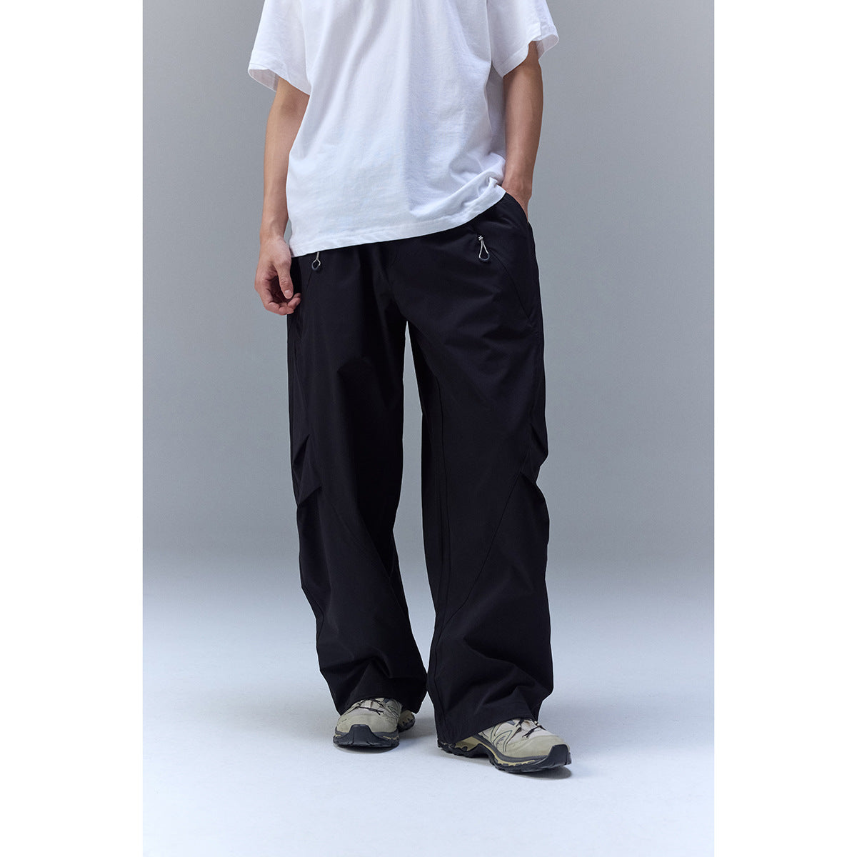 Model wearing loose black outdoor pants with a white T-shirt and drawstring pocket details.