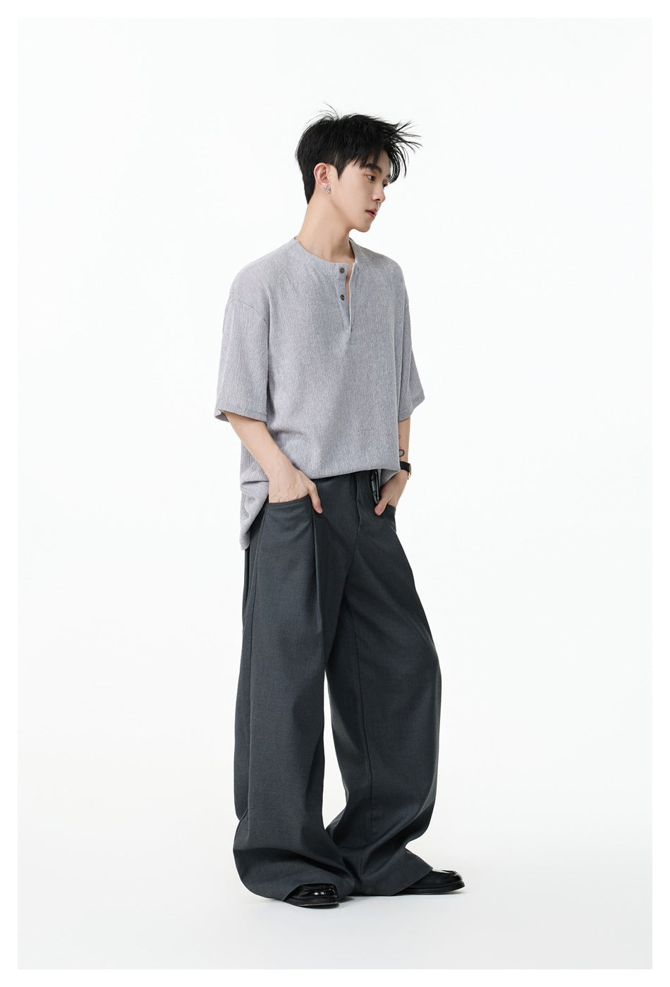 Model wearing a light gray textured Henley-collar tee with wide-leg dark gray trousers, side view