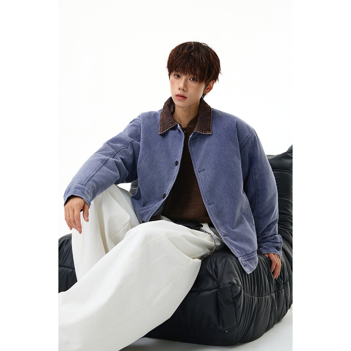 Model seated in a blue-violet button-front jacket with a brown collar and white trousers.