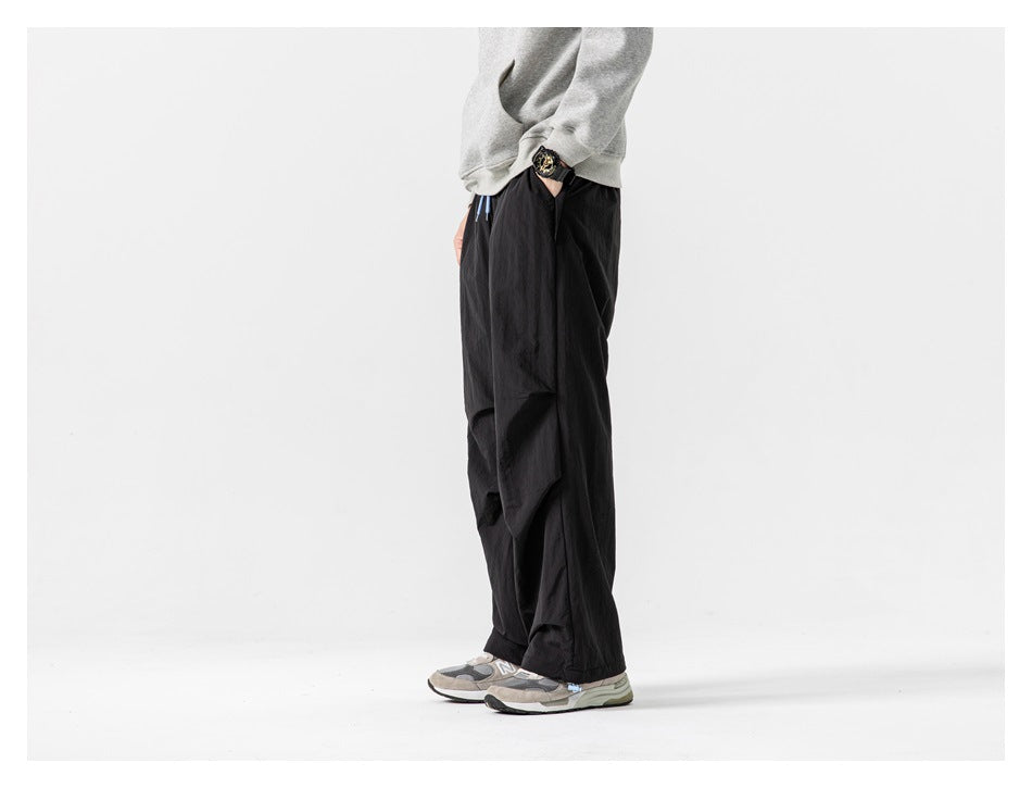 Side view of a model wearing loose black pants with a large side pocket and sneakers.