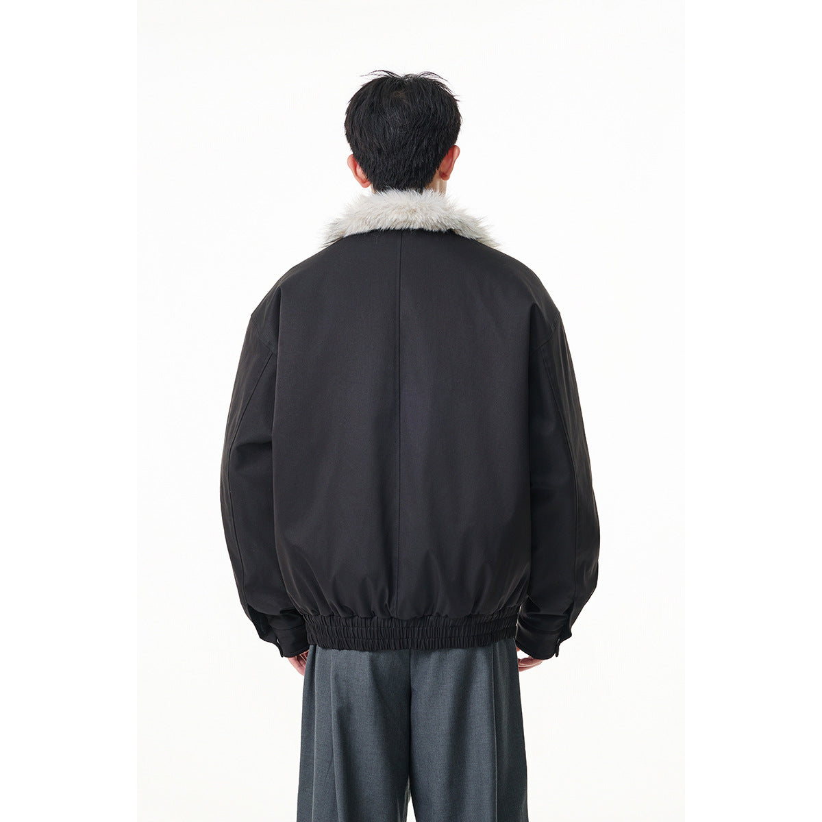 Back view of a black jacket with a light gray fur collar and gathered elastic hem, worn with dark trousers.