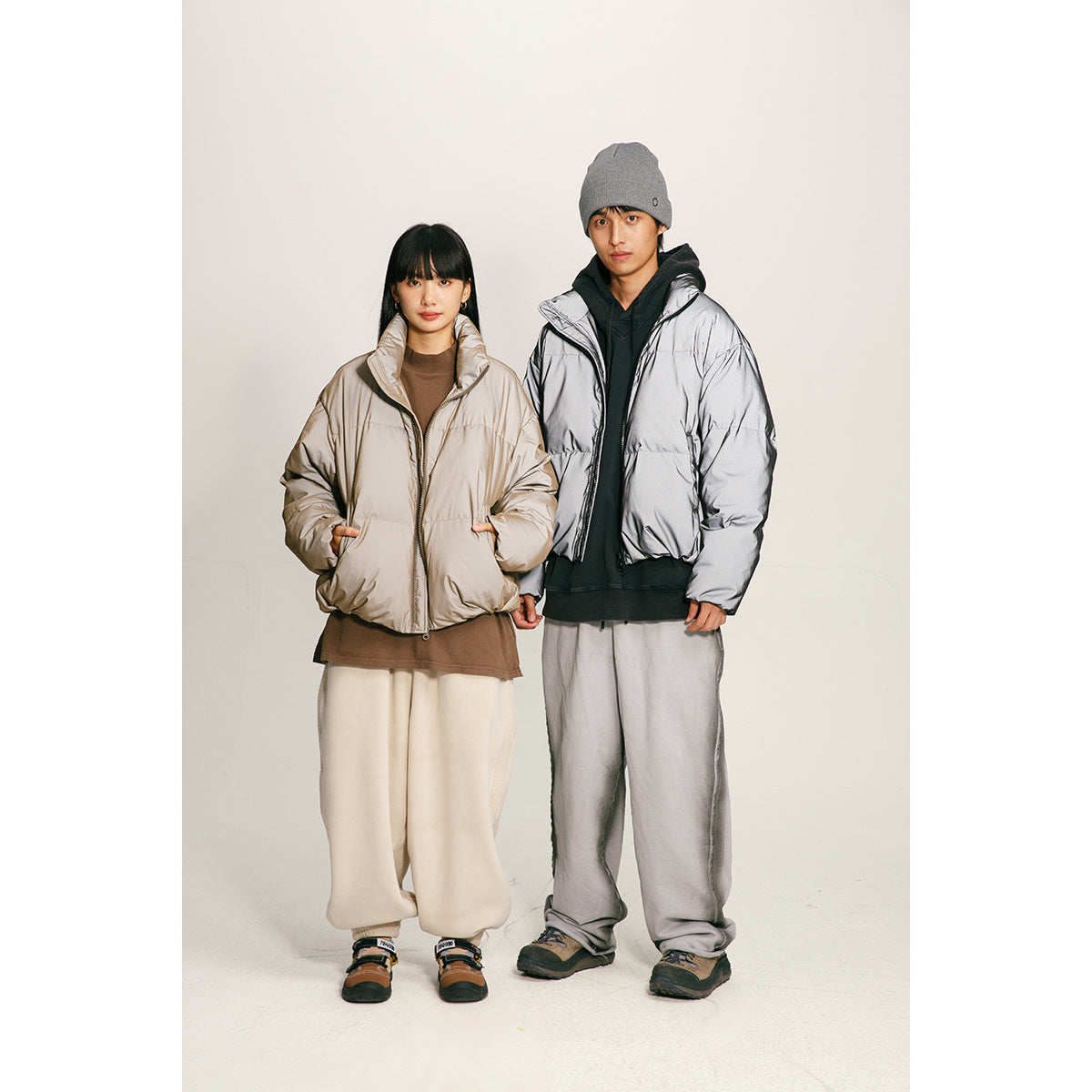 Two models wear a taupe puffer jacket and a silver puffer jacket against a plain studio background.