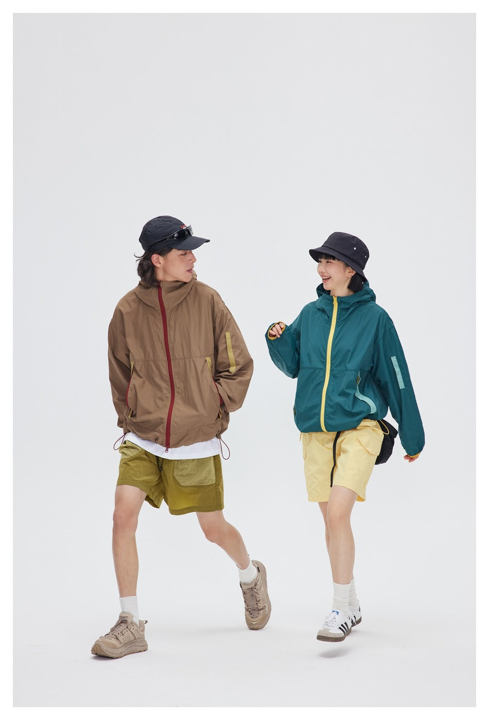 Two models walking in taupe and teal hooded jackets with contrasting zipper and pocket accents.