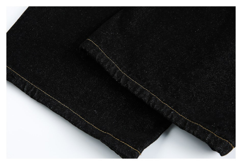 Close-up of black jean leg hems with golden stitching.