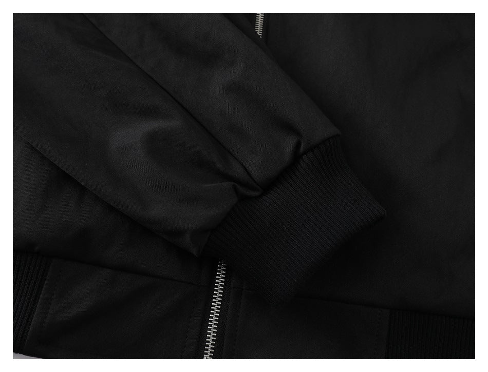 Close-up of a black jacket showing a ribbed sleeve cuff, ribbed hem, and silver zipper.