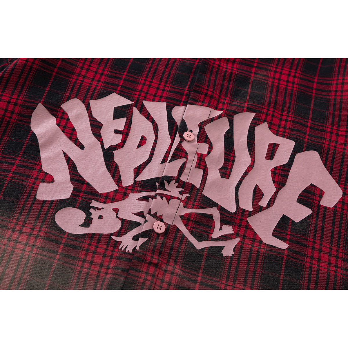 Close-up of red-and-black plaid shirt fabric with large pale graphic lettering and an illustrated figure.