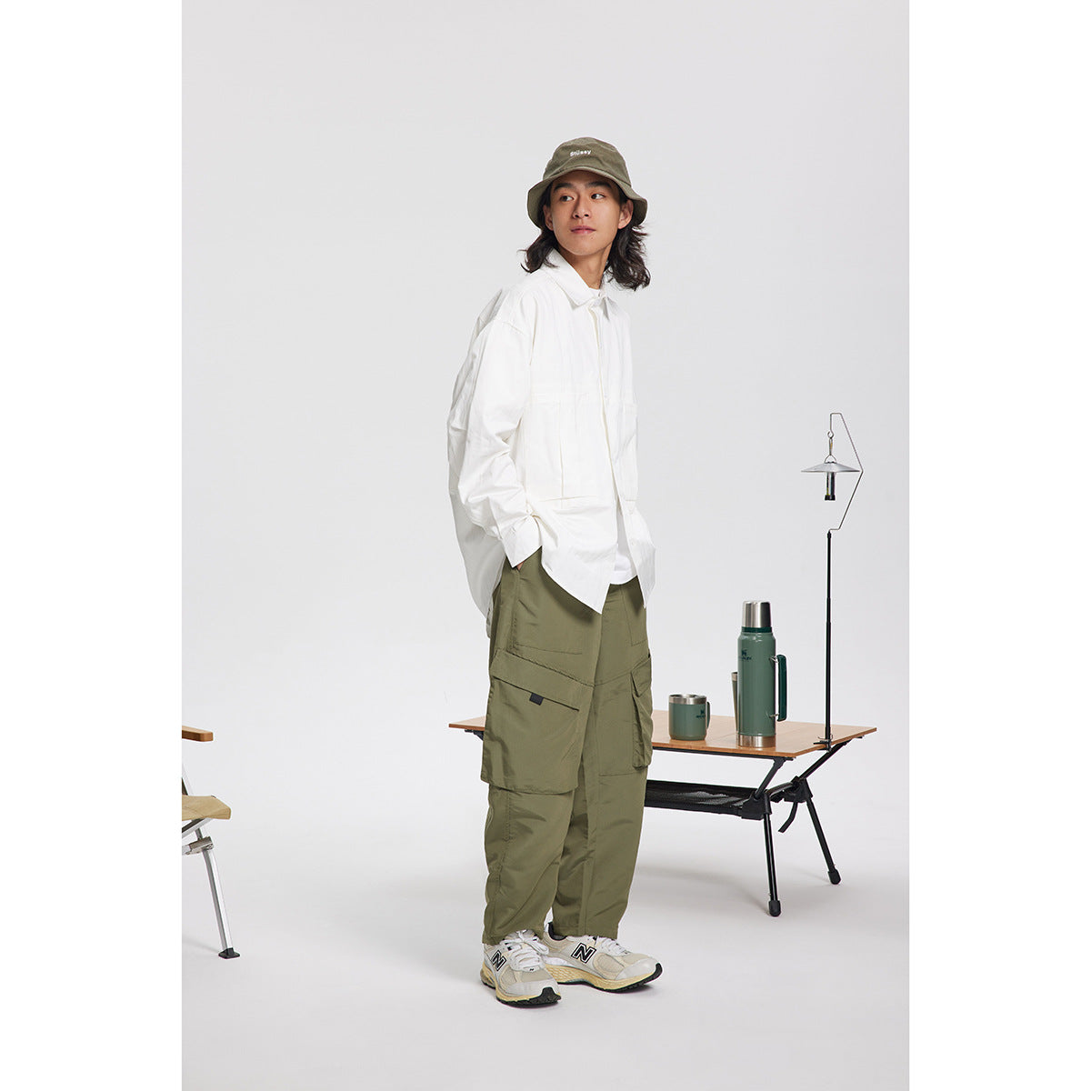Model wearing an oversized white button-up shirt, olive cargo pants, and an olive bucket hat.