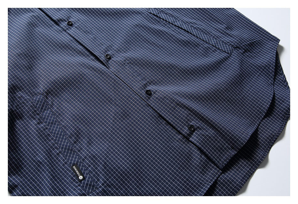 Close-up of a navy check shirt front with black buttons and a chest pocket.