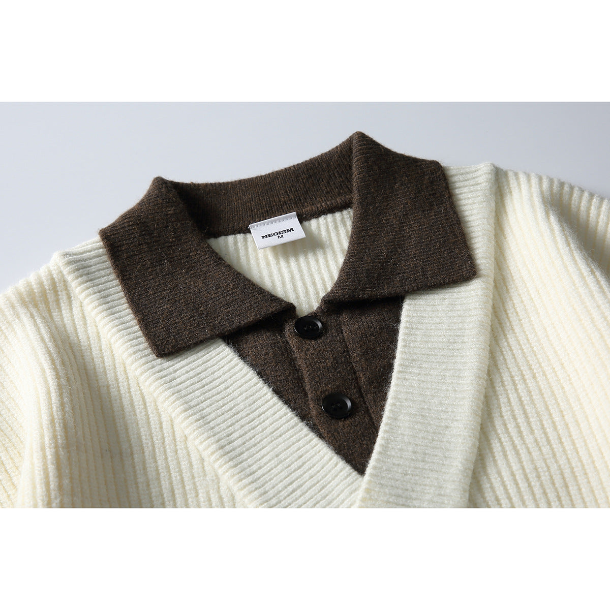 Close-up of an ivory ribbed sweater with a dark brown collared placket and two black buttons.