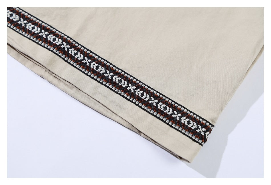 Close-up of a beige shirt hem with a diagonal band of black, white, and rust geometric trim.