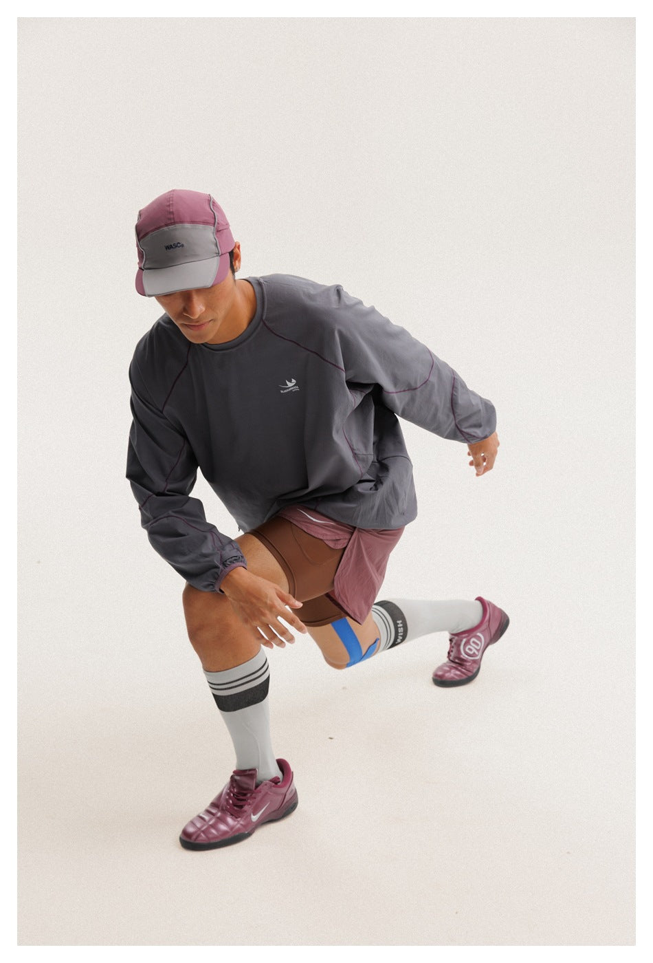 Model in motion wearing a charcoal gray pullover with plum contrast seams and mauve shorts over brown fitted shorts.