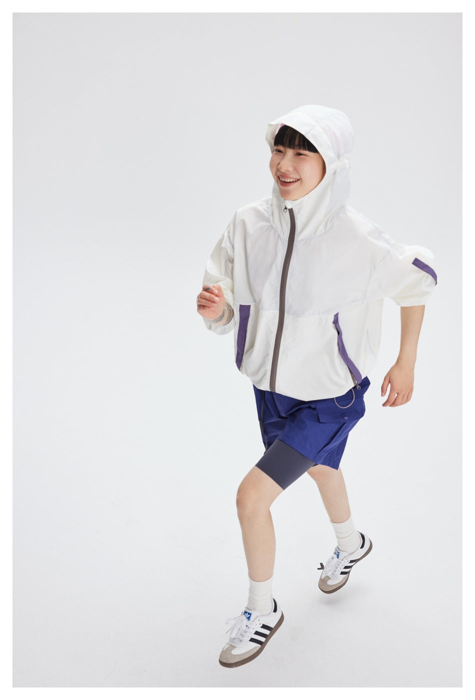 Model in a white hooded jacket with purple accents and blue shorts, shown in a running pose.