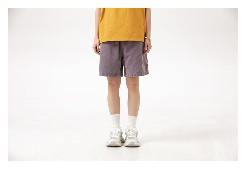 Front view of a model wearing muted purple-gray shorts with a mustard yellow top, white socks and sneakers.