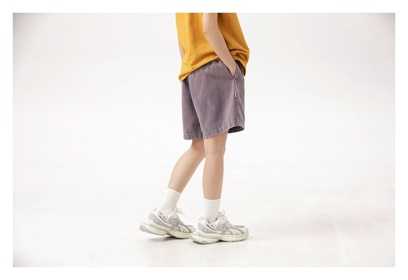 Cropped side view of a person wearing muted purple-gray shorts with a mustard T-shirt and white socks.