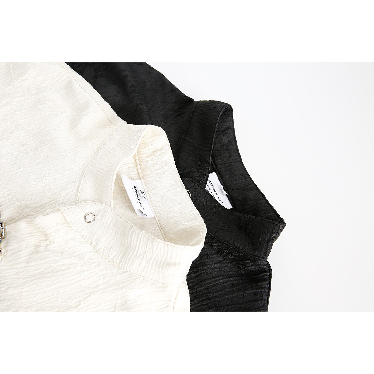 Close-up of ivory and black mandarin-collar shirts showing the collars, inner labels and textured fabric.