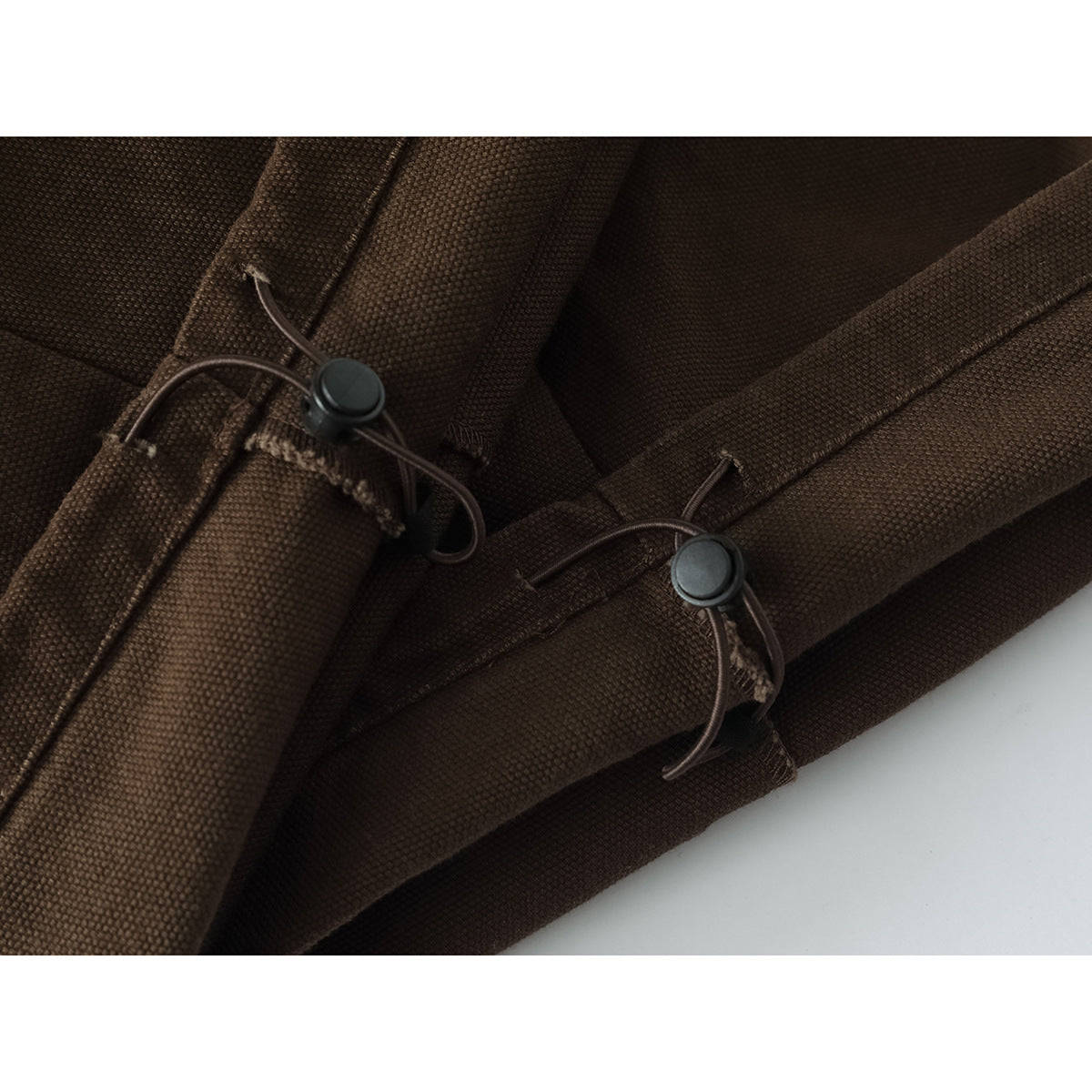 Close-up of brown trouser hems with adjustable elastic cords and round toggles.