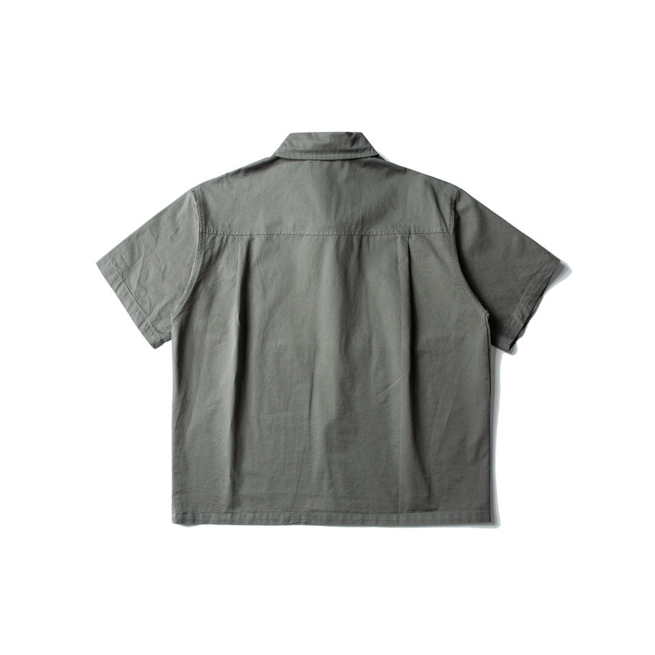 Back view of a gray-green short-sleeve button-up shirt with a folded collar and a pleated back yoke.