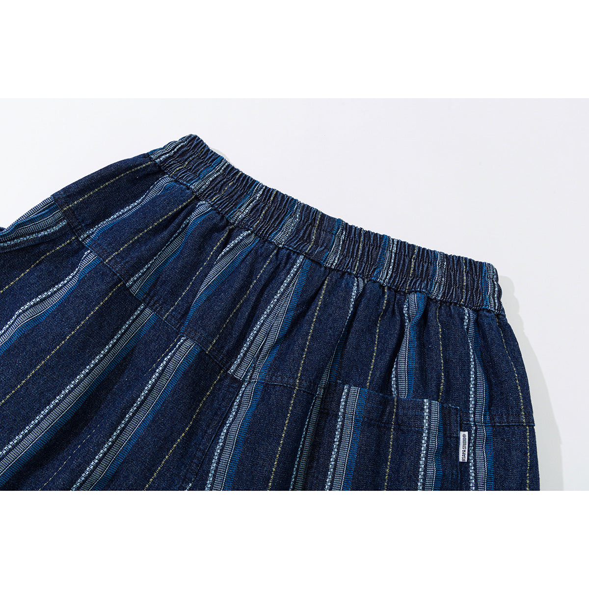 Close-up of dark blue striped trousers showing the elastic waistband, pocket stitching, and a small sewn label.