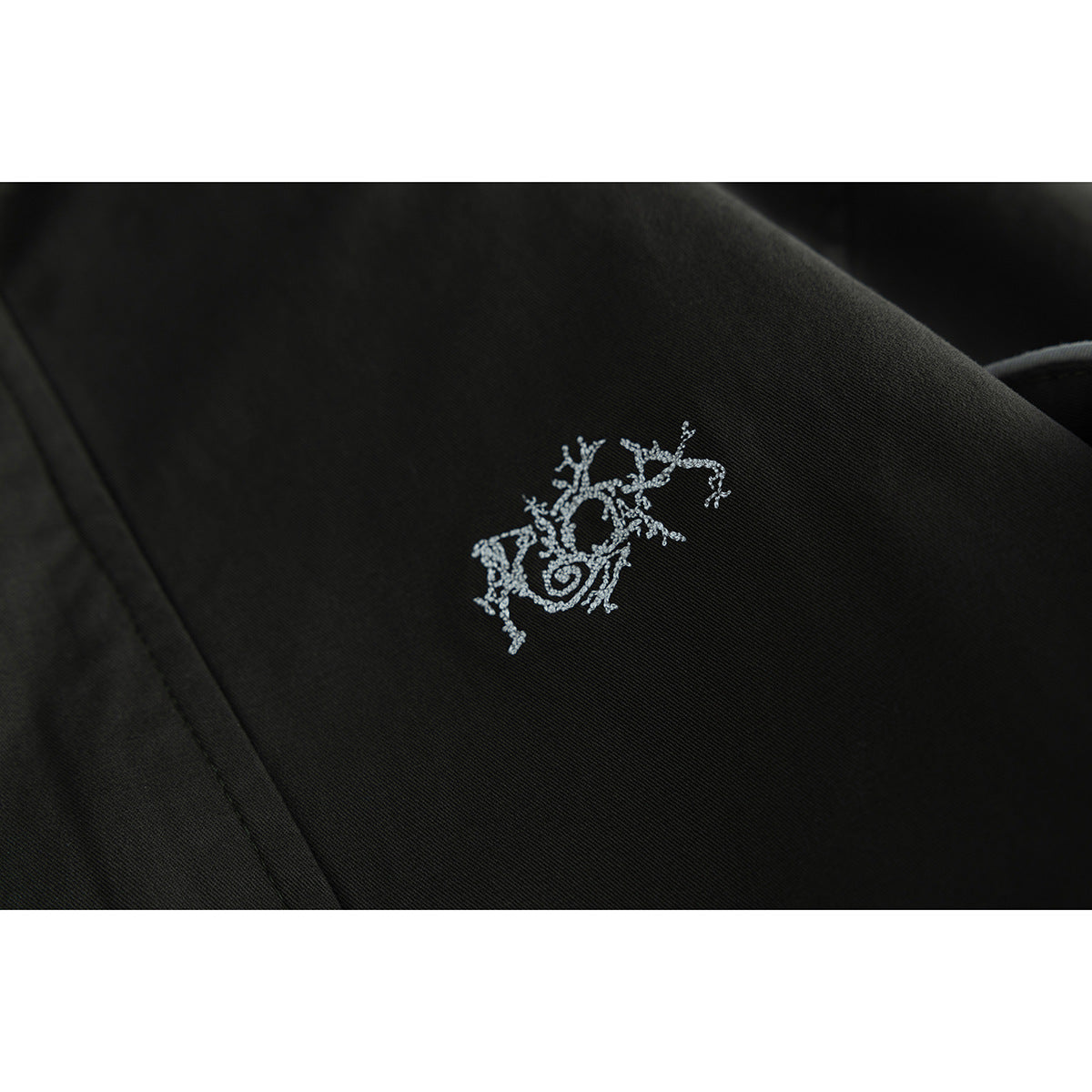 Close-up of a small white embroidered motif on dark jacket fabric.