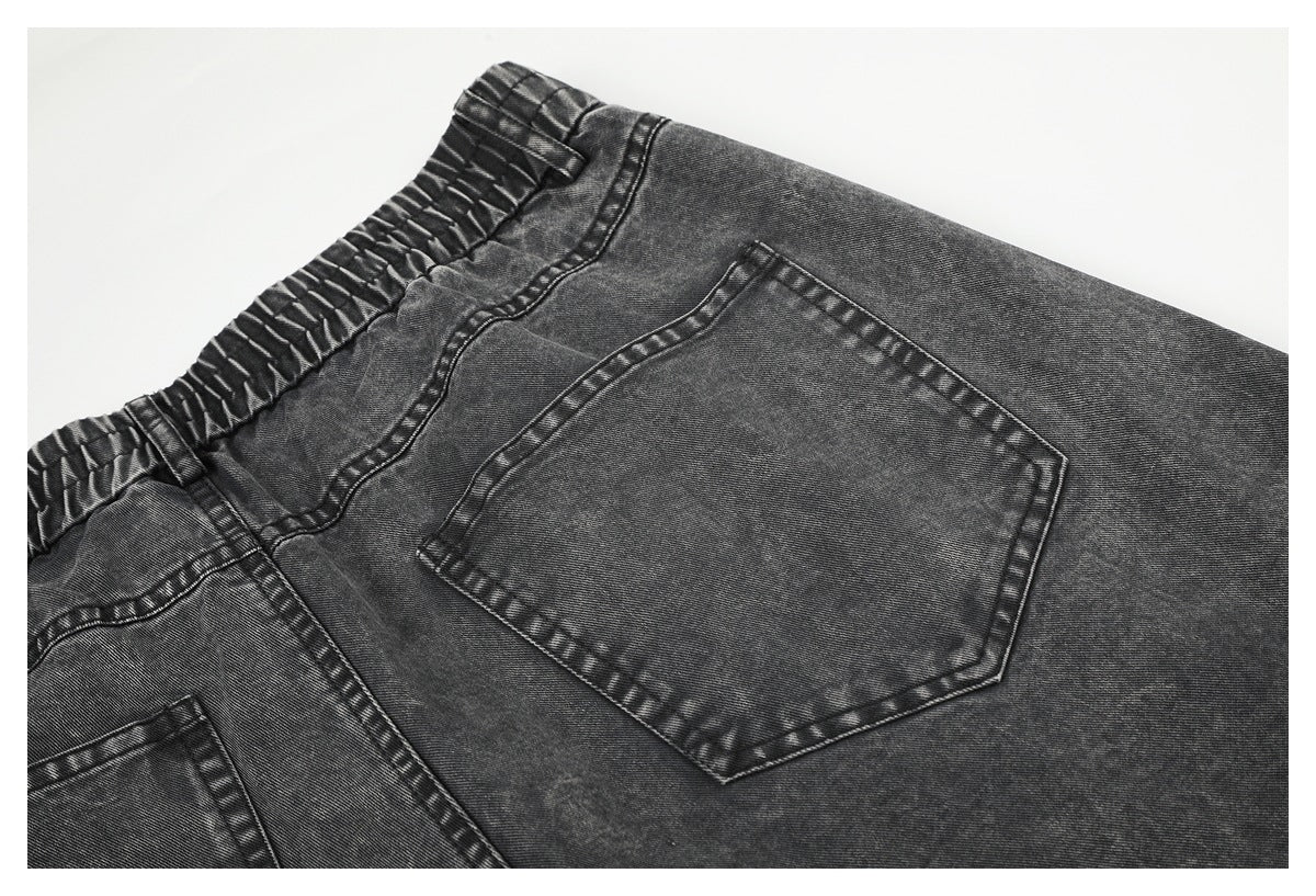Close-up of charcoal gray jeans showing the gathered elastic waistband and a rear pocket.