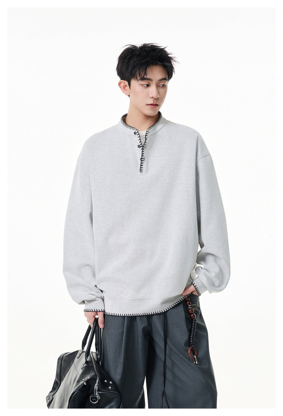 Model wearing a light gray oversized pullover with black contrast stitching at the placket, cuffs and hem.