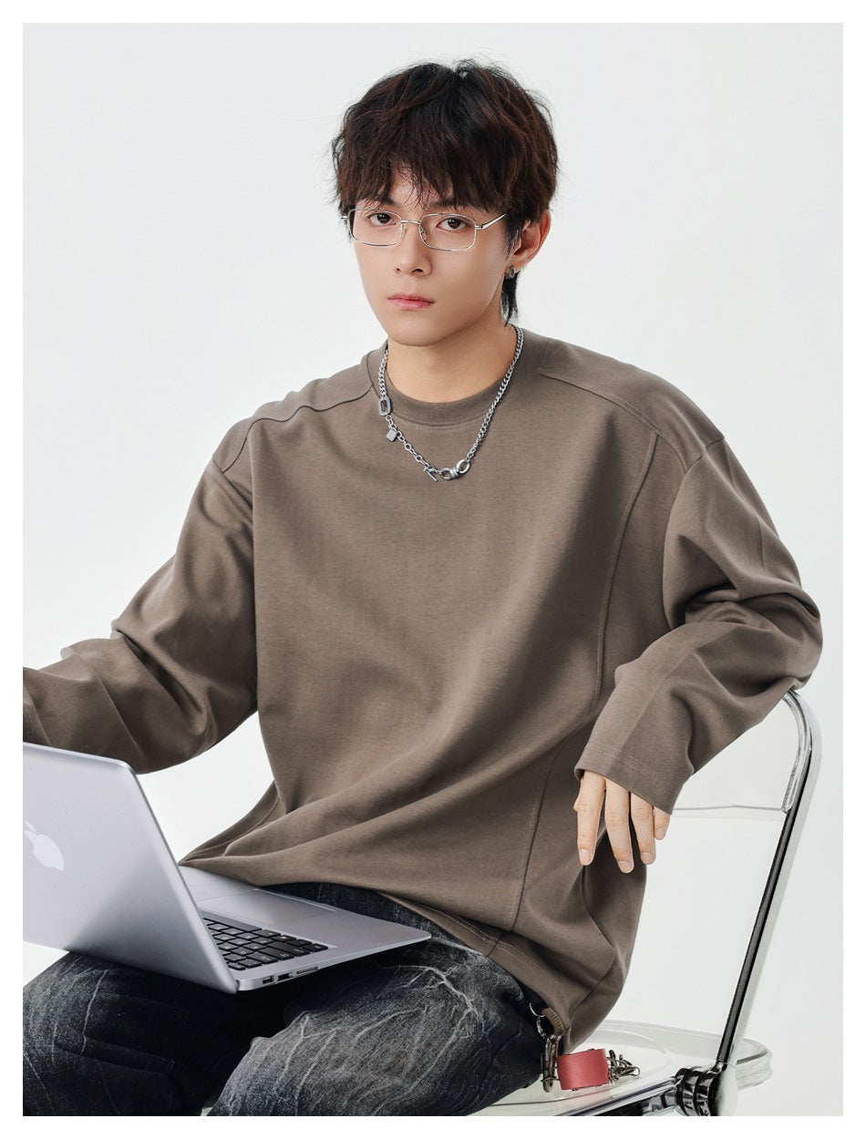 Seated model wearing a taupe oversized long-sleeve crewneck top with seamed shoulders.