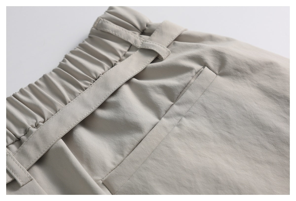 Close-up of a gathered light taupe waistband with a matching belt and a stitched side pocket.