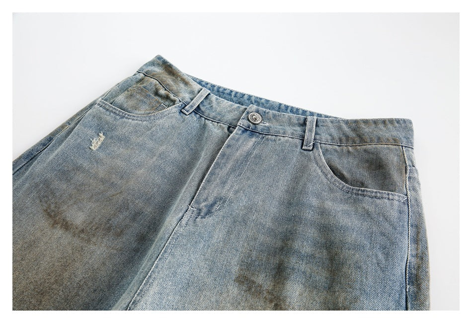Close-up of the jeans' waistband, button, front pockets and faded wash with a small distressed mark.