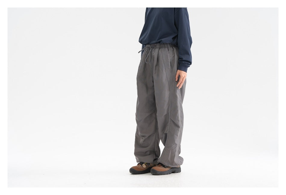 Side-front view of a model wearing loose charcoal gray drawstring pants with piping.