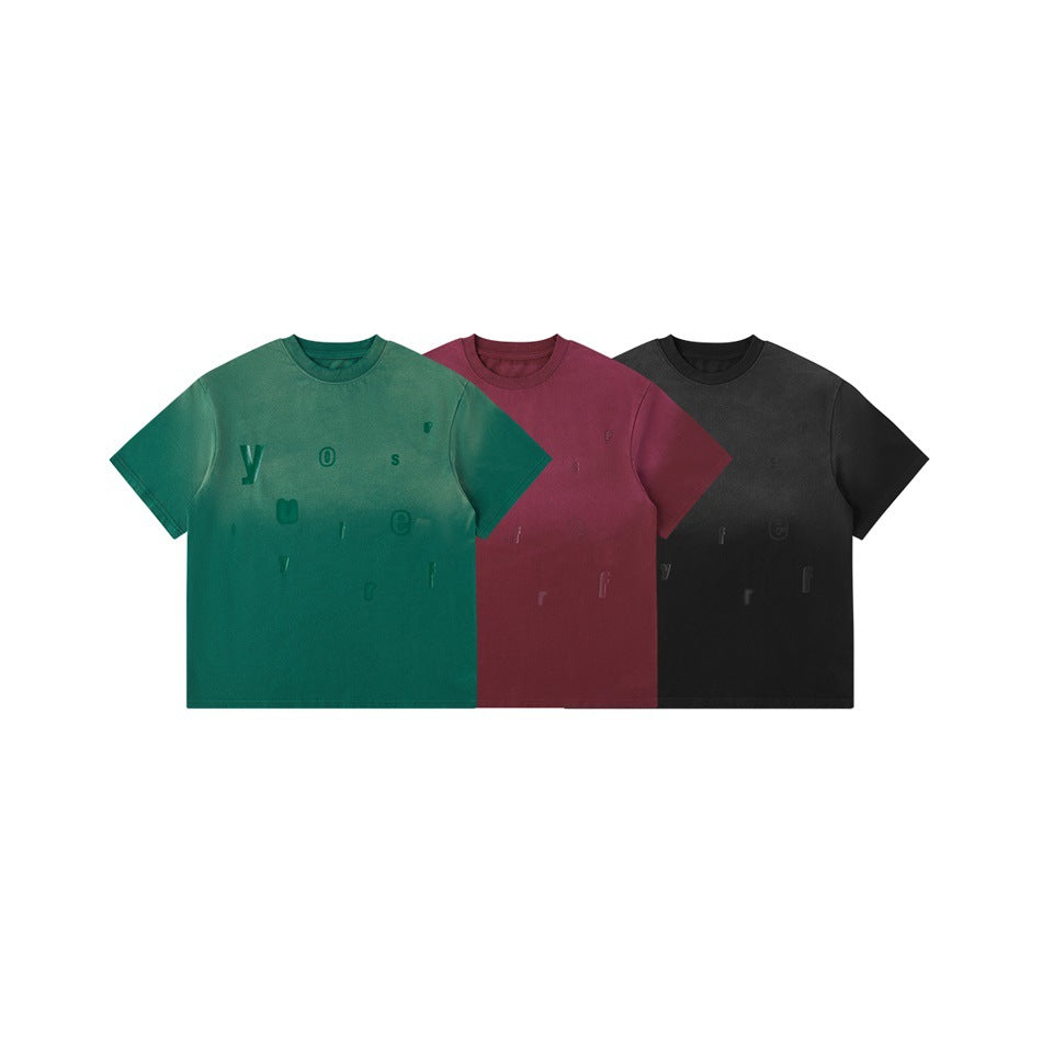 Fronts of three short-sleeve crew-neck T-shirts in green, burgundy, and black with scattered letter graphics.