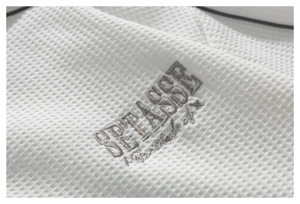 Close-up of white textured fabric with gray embroidered lettering.