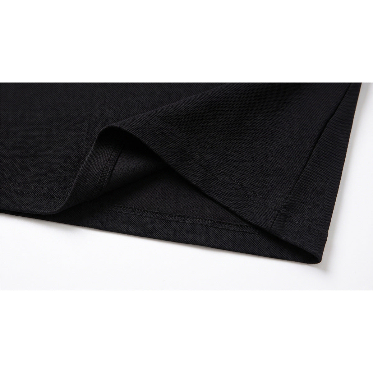 Close-up of the black polo's folded hem and stitched seam against a white background.
