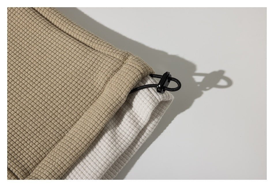 Close-up of a beige jacket hem with a black drawcord toggle and white lining.