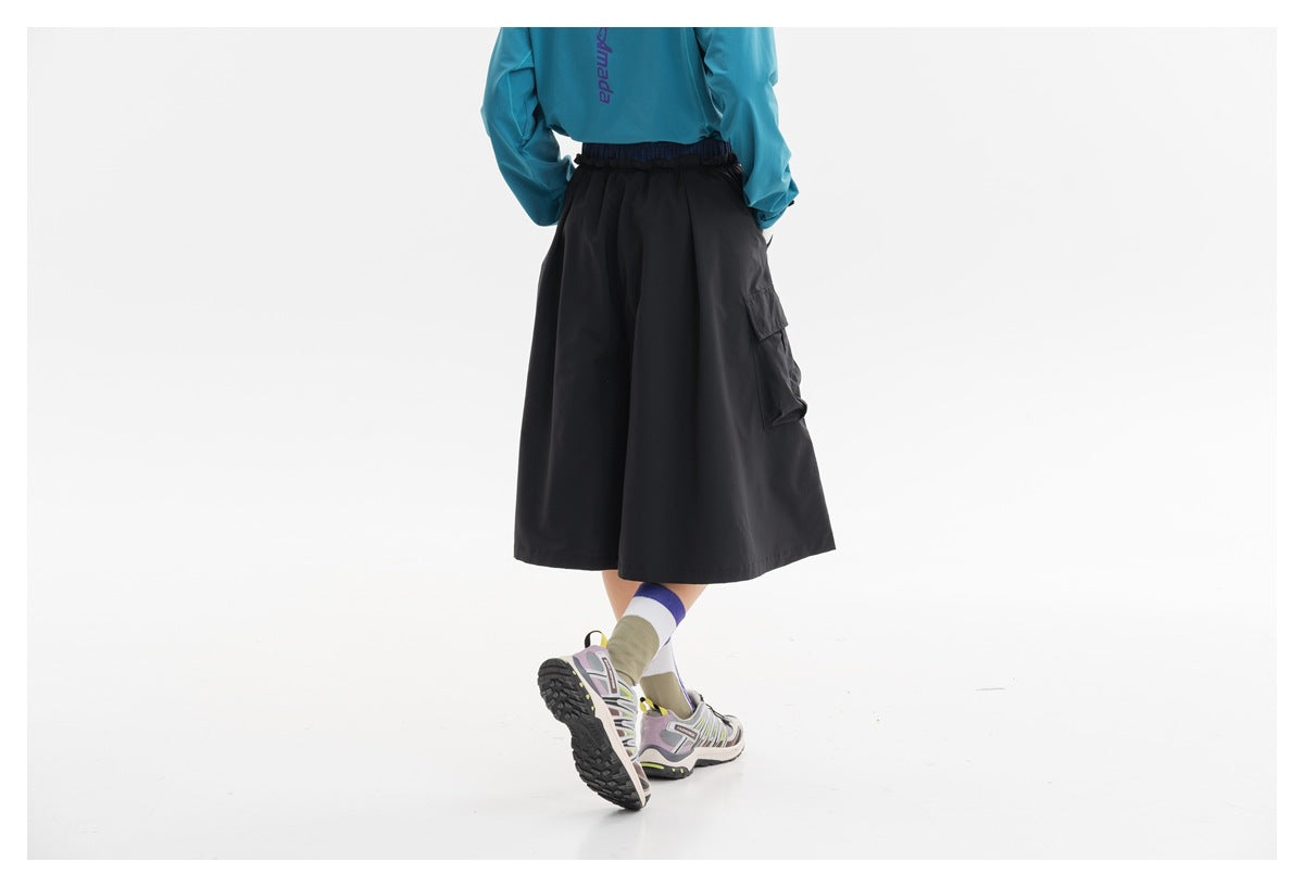 Back view of a black flared cargo skirt with an elastic waist and side pocket, worn with a teal top.
