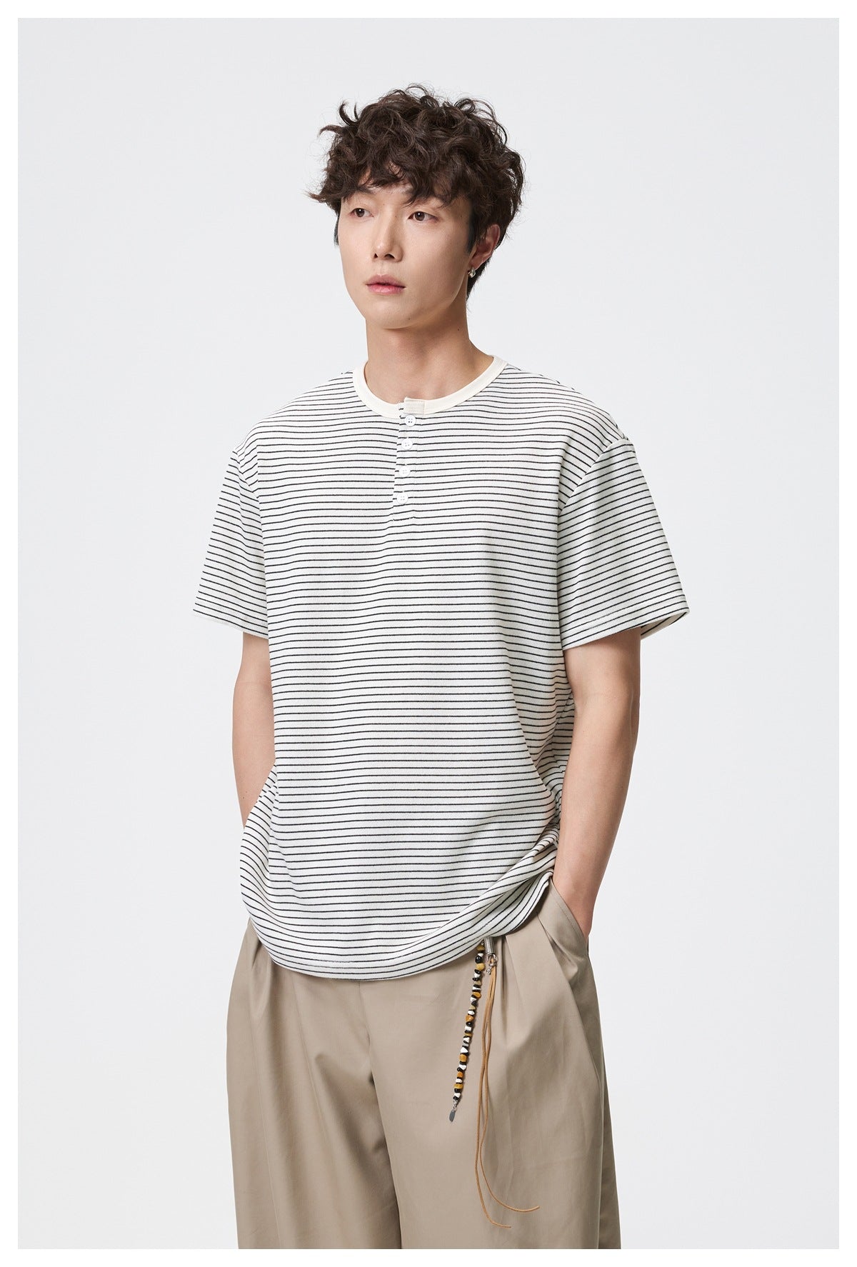 Three-quarter view of a model wearing an ivory, thin black-striped Henley T-shirt with beige trousers.